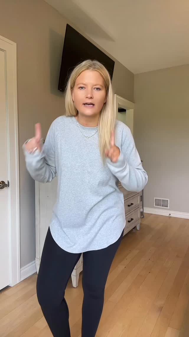 How to Style a Tunic: 9 Ideas From Jeans to Shorts 3 Woman wearing a long grey tunic top paired with black leggings in a room.