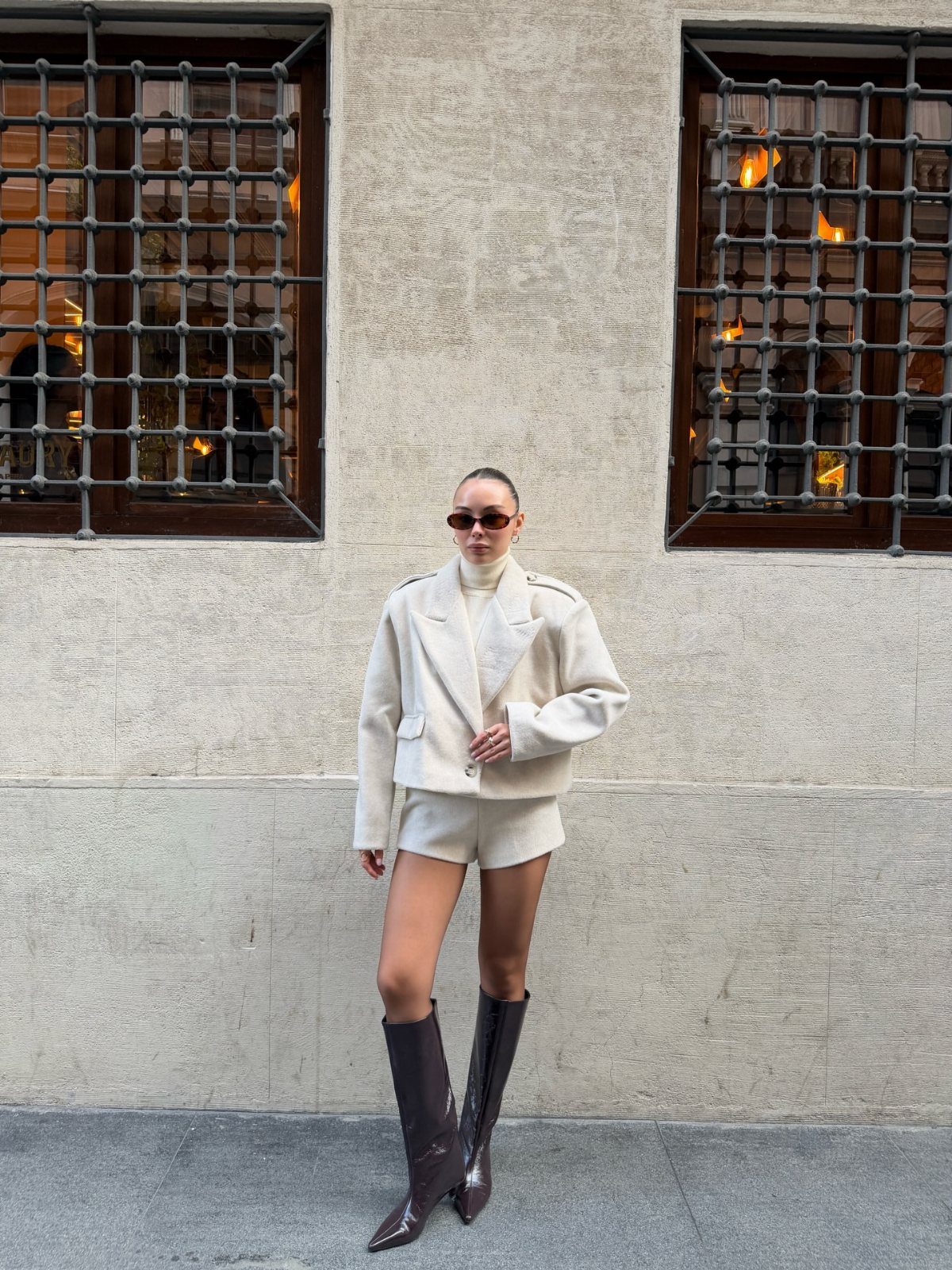 Woman wearing a white jacket and white shorts with brown knee-high boots.
