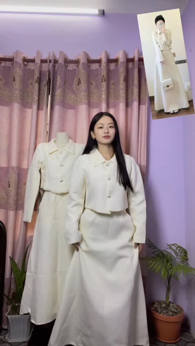 Woman wearing a white cropped jacket and matching long white skirt in a room.