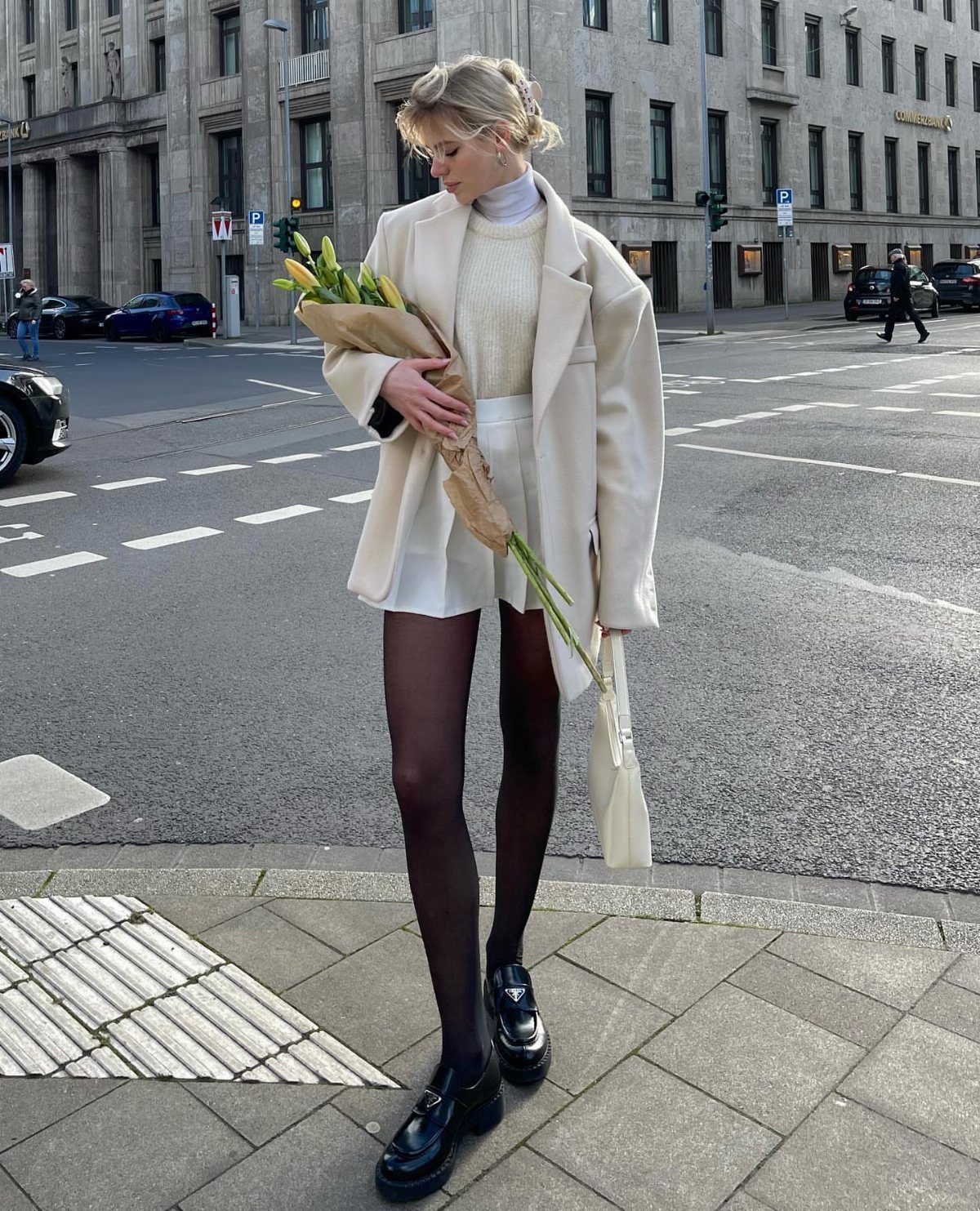 Woman in white jacket and white skirt holding yellow tulips on city street