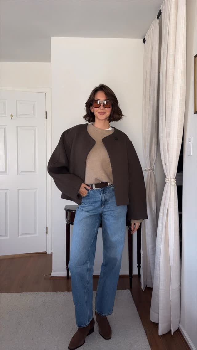 Woman wearing a beige sweater, blue jeans, and brown boots in a room.