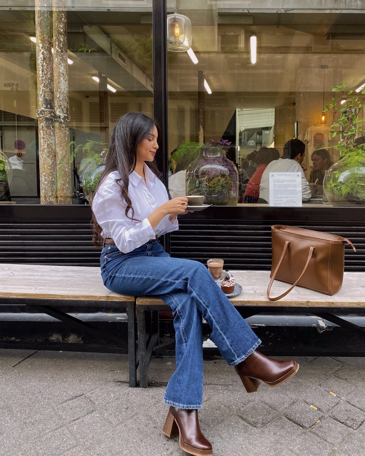 Woman wearing wide-leg blue jeans and brown leather boots sitting on a bench.
