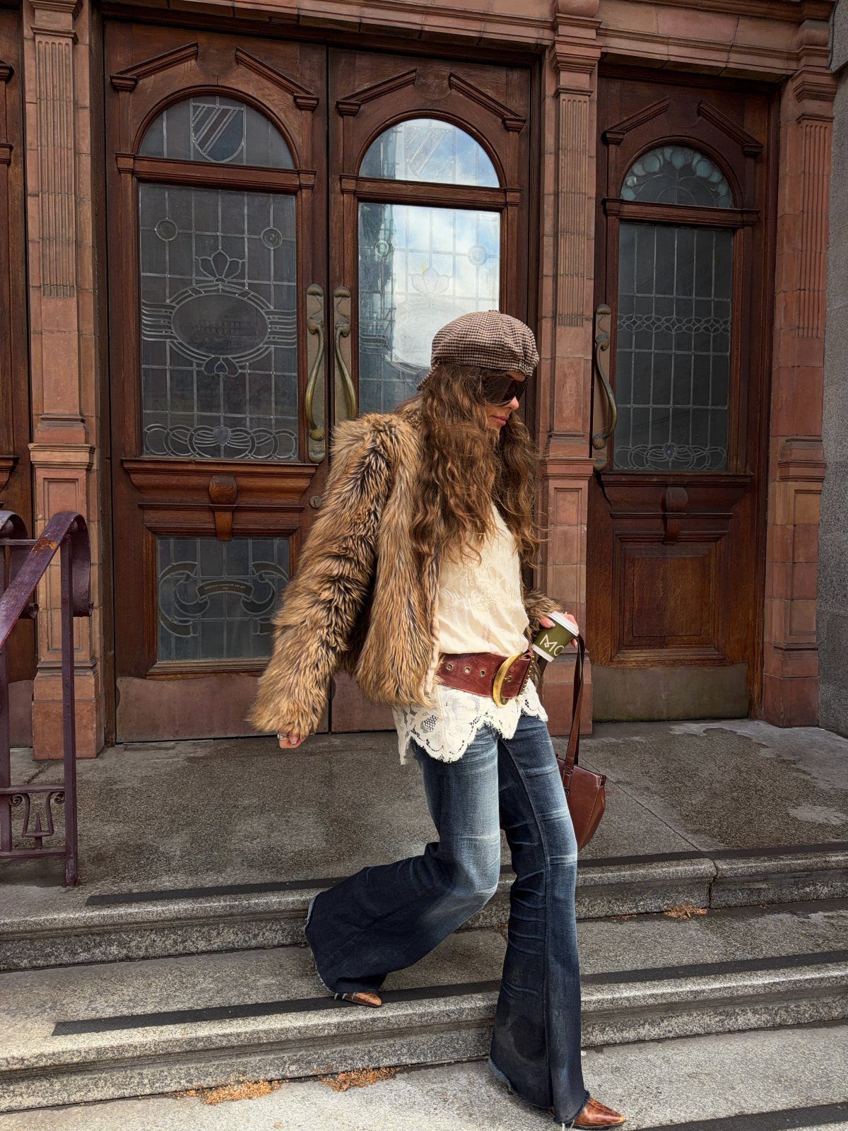 Woman in flared blue jeans and brown boots wearing a faux-fur jacket.
