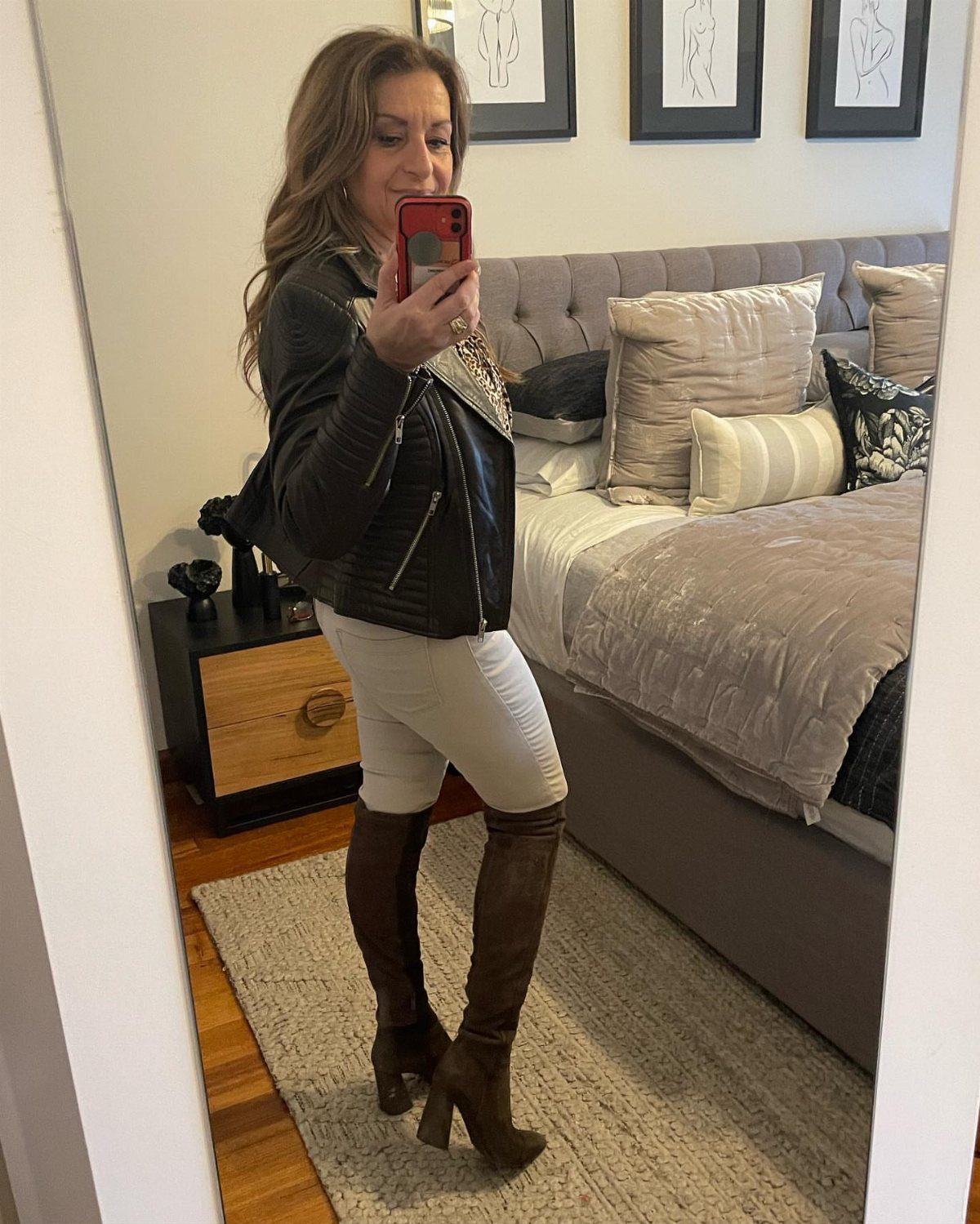 Woman wearing white skinny jeans and tall brown heeled boots in a bedroom.