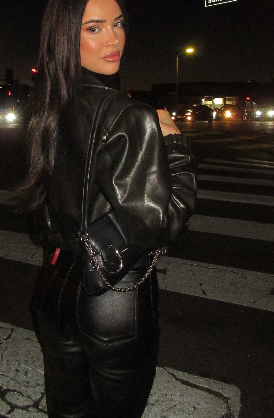 Woman in black leather jacket and leather trousers standing on a city street.