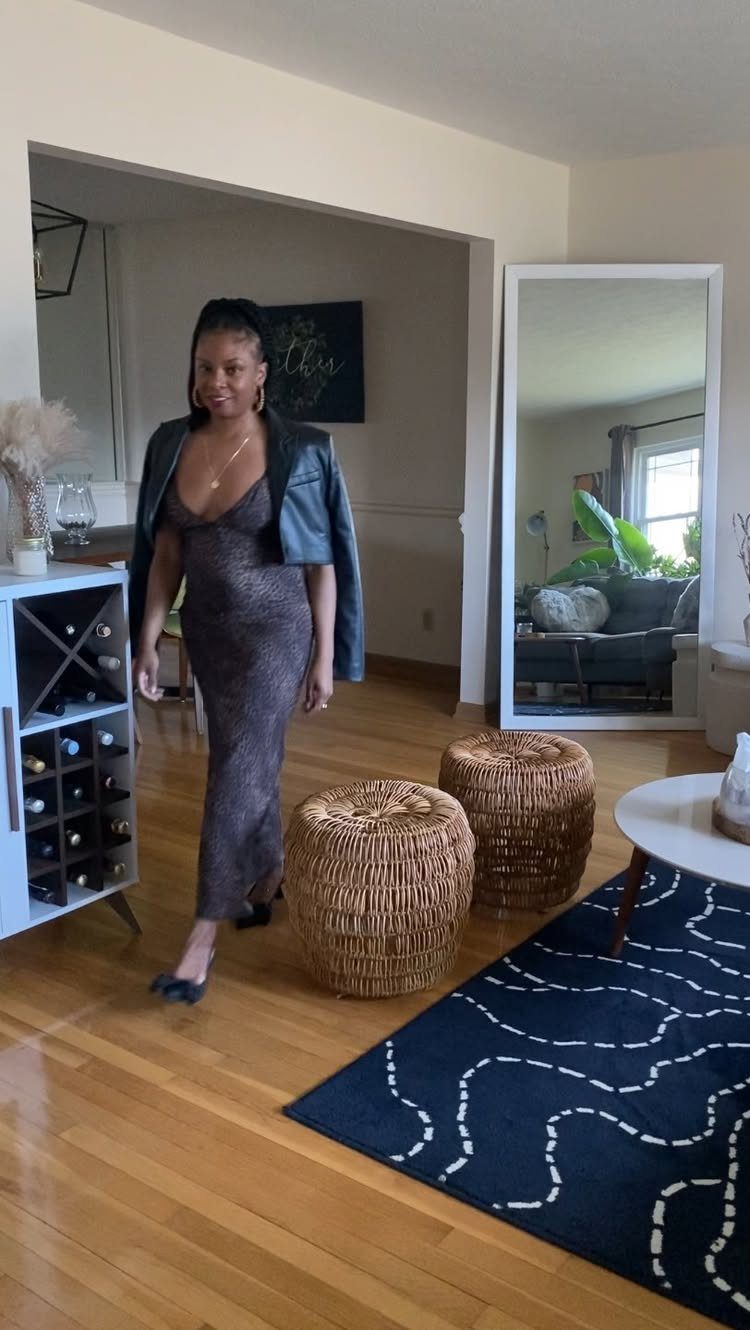 Woman in a shimmering long dress and black leather jacket posing in a living room.