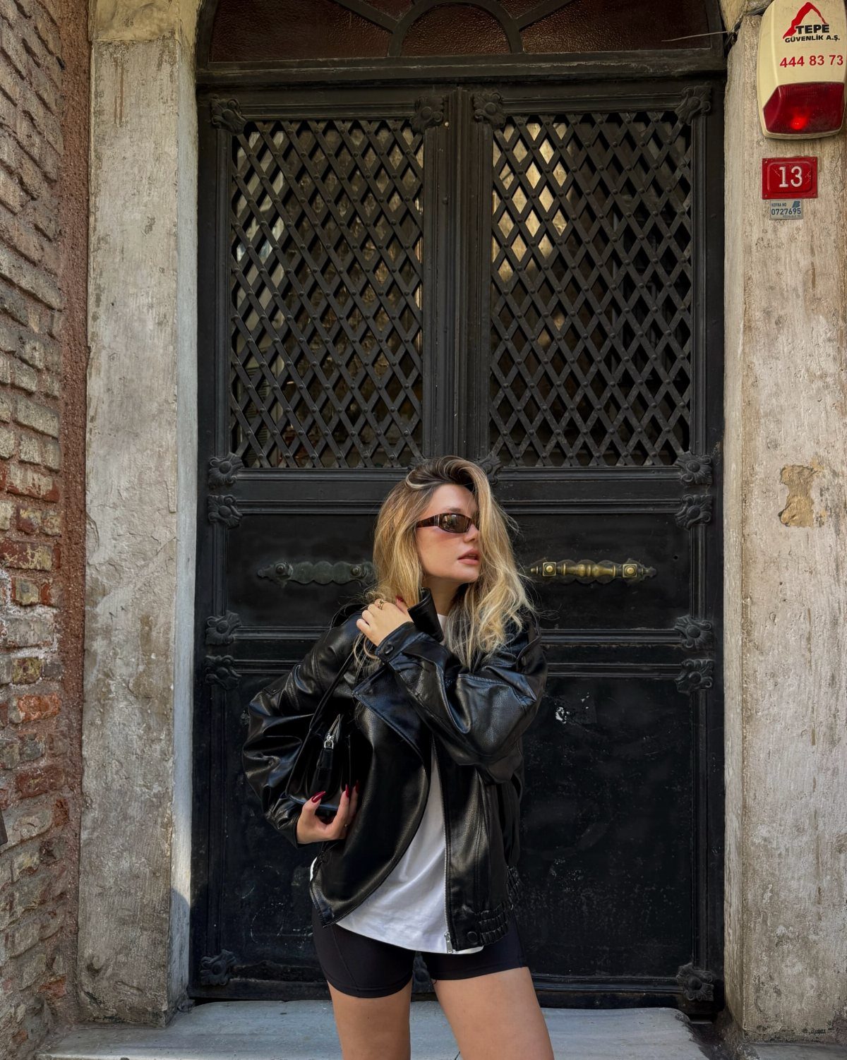 Woman in black leather jacket and white t-shirt posing by ornate black door.