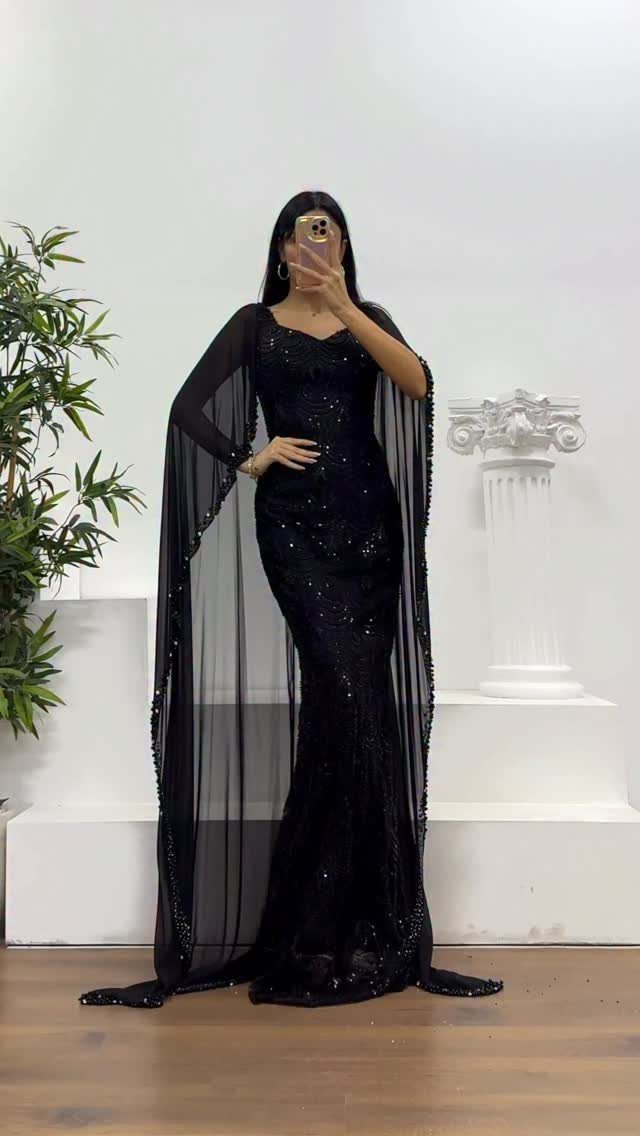10 Luxury Dress for Wedding Guest Ideas and Styles 6 Woman in a shimmering black formal gown with a sheer floor-length cape.