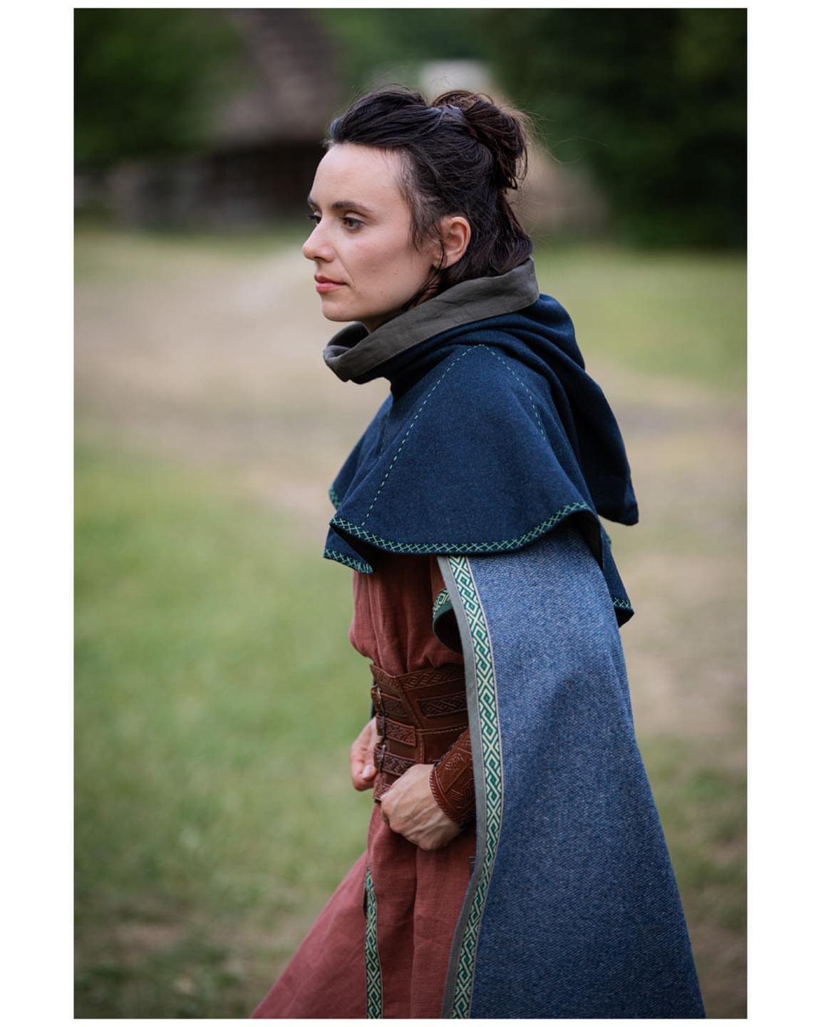 Woman wearing a red medieval dress and a blue wool cloak in a field