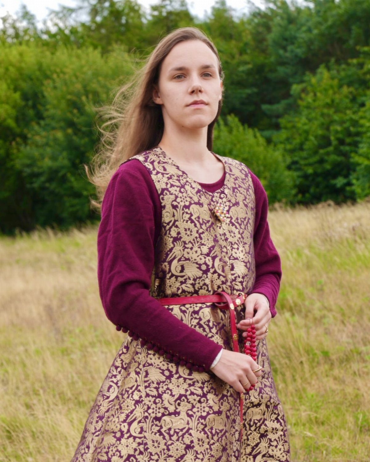 Medieval Period Dress: 12 Women's Styles and Looks 10 Woman wearing a purple and gold patterned medieval dress in a grassy field