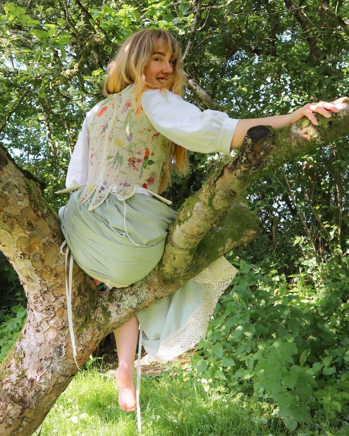 Medieval Period Dress: 12 Women's Styles and Looks 8 Woman in medieval-style floral vest and green skirt sitting on a tree branch