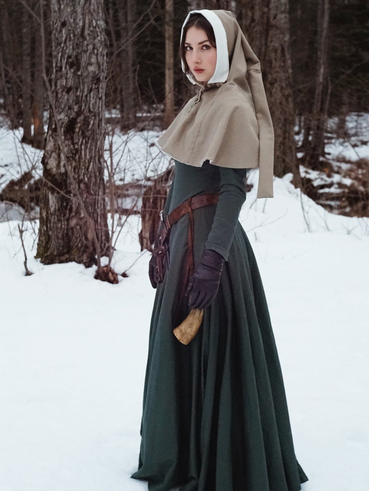 Medieval Period Dress: 12 Women's Styles and Looks 11 Woman in a green medieval dress wearing a tan wool hood in snowy woods