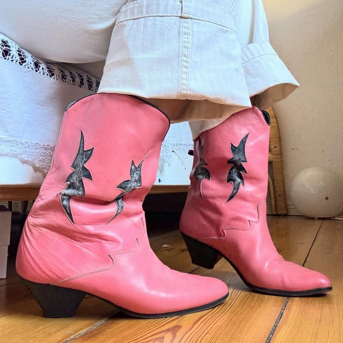 Pink leather cowboy boots with black flame patterns and white cuffed trousers.