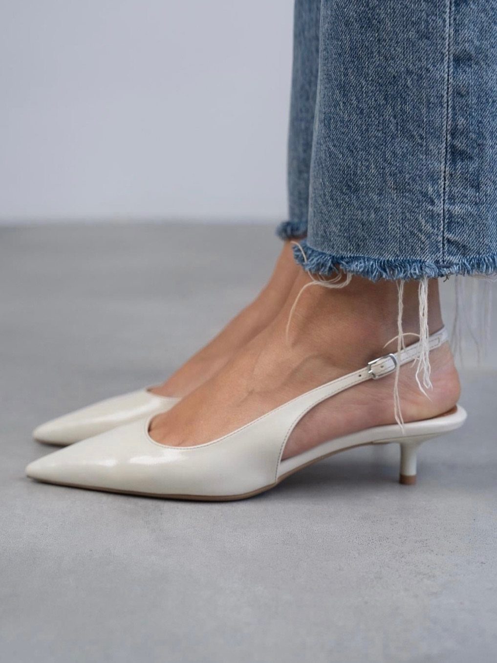 White pointed-toe kitten heels with slingback straps worn with blue frayed denim jeans.