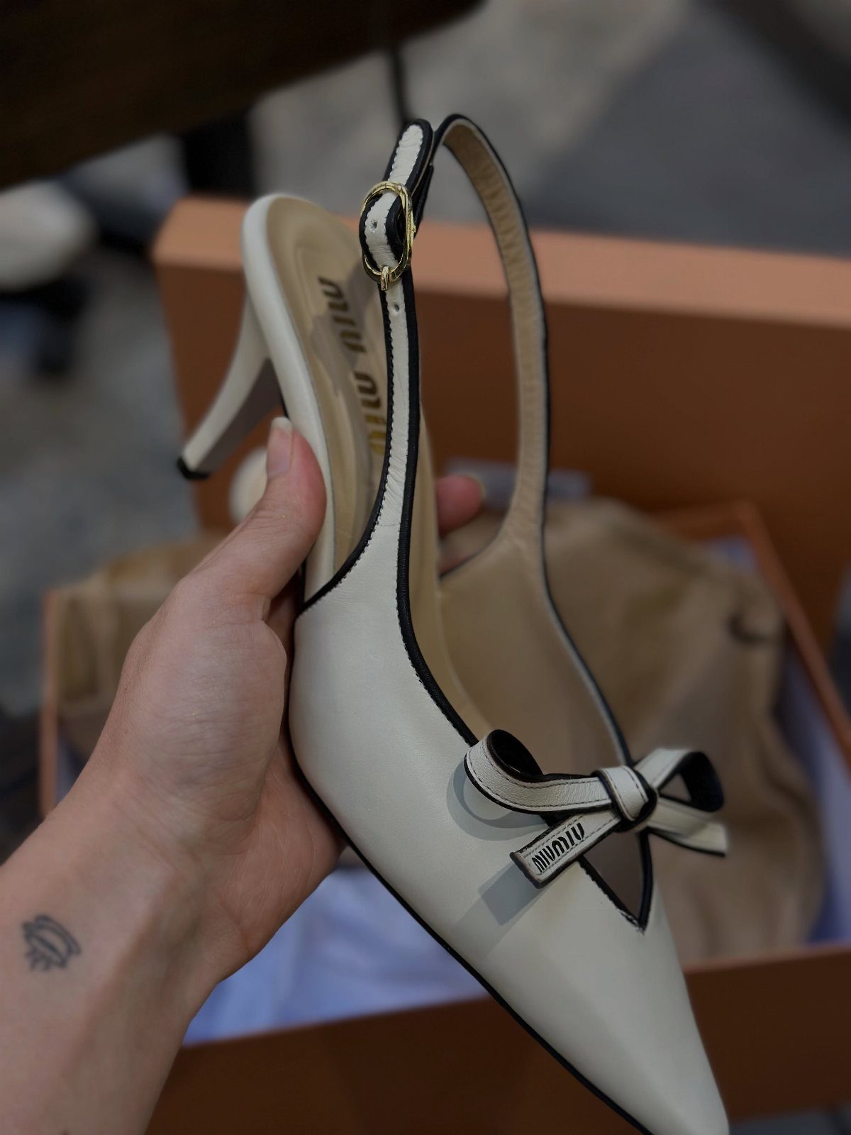 Miu Miu Kitten Heels: 7 Ideas for Every Outfit 4 White leather slingback kitten heels with a bow and black piping held by hand.