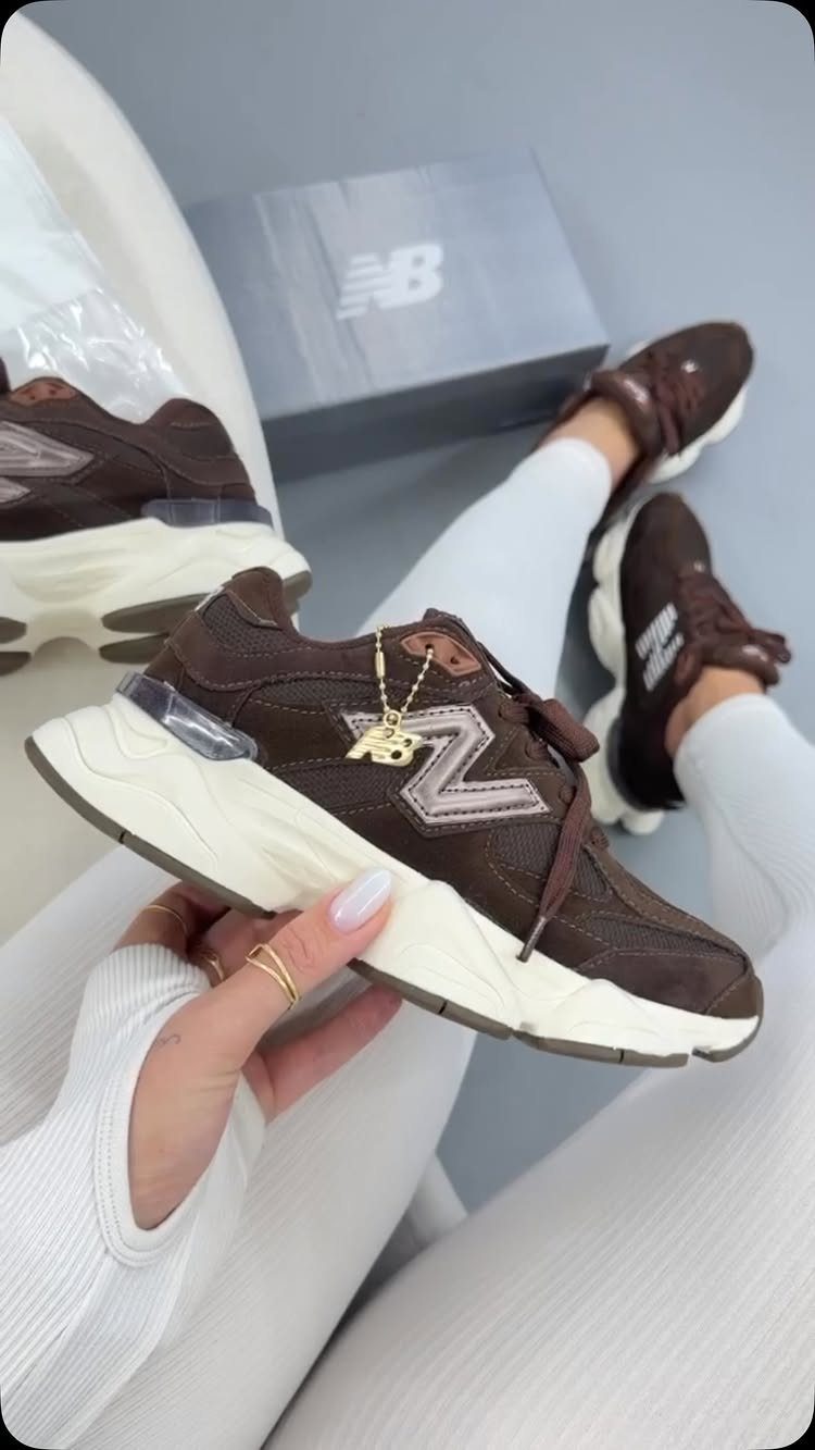 Brown New Balance 9060 sneakers held by a person wearing white ribbed leggings.