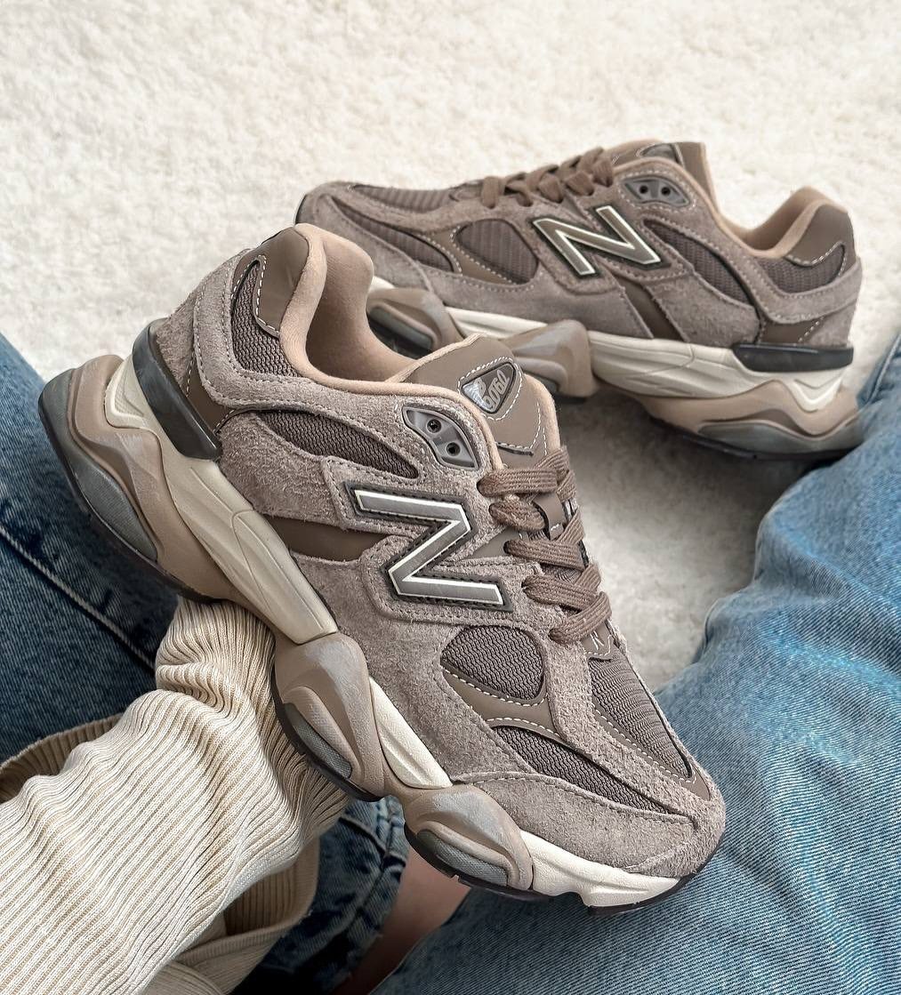 Brown New Balance 9060 sneakers worn with blue jeans on a white carpet.