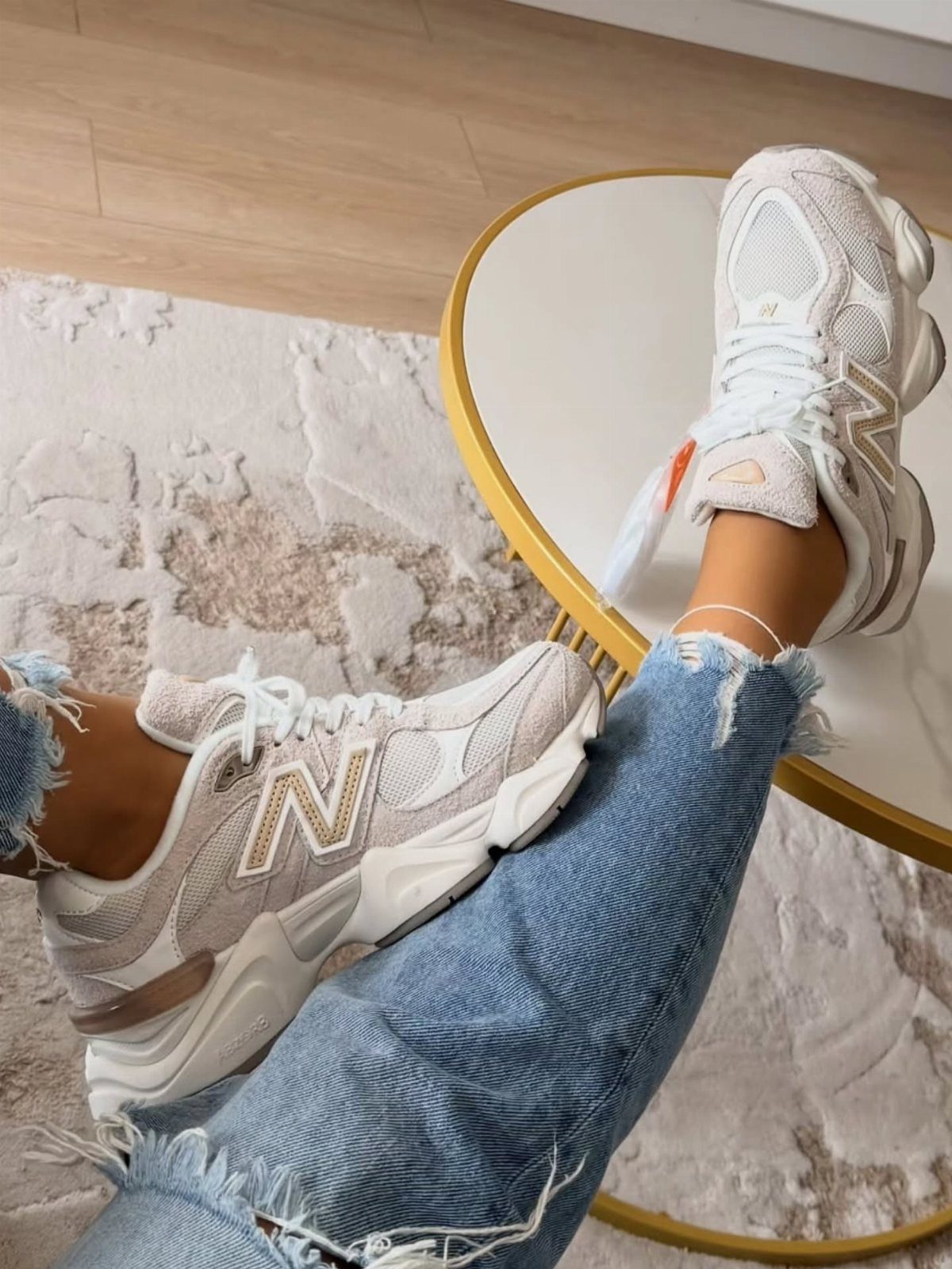 Beige New Balance 9060 sneakers worn with ripped blue jeans on a table.