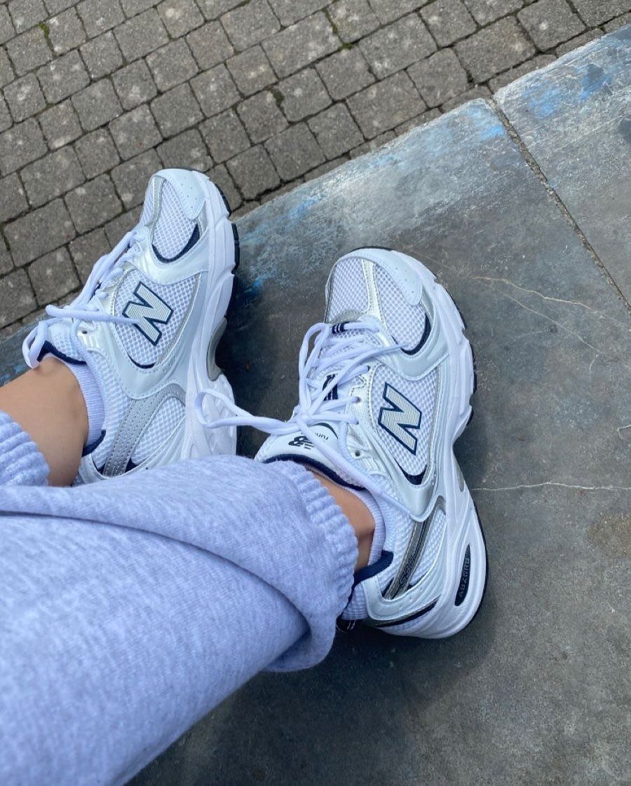White New Balance sneakers with mesh panels and silver accents on grey pavement