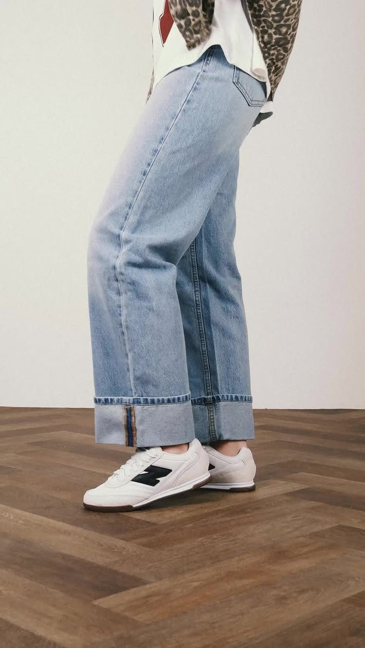 White New Balance sneakers paired with light blue cuffed denim jeans on wood floor