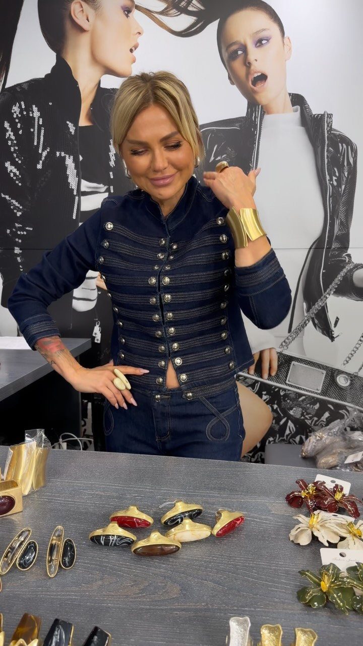 Woman wearing a gold cuff bracelet standing behind a display of chunky rings.