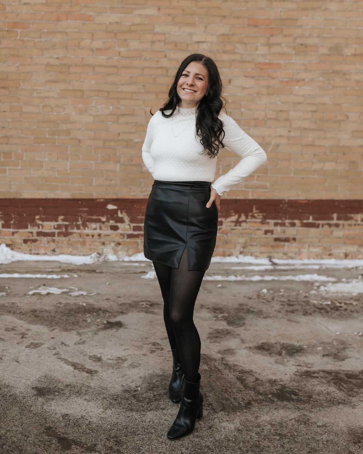 Woman wearing a white top and black faux leather mini skirt with boots.