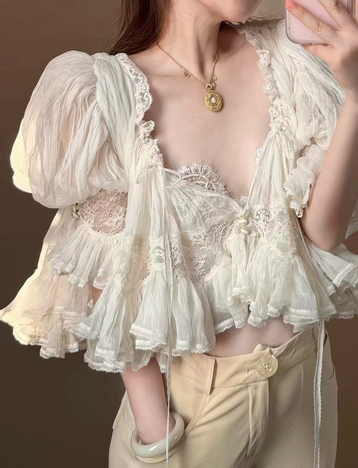 White ruffled cropped blouse with lace and puff sleeves paired with cream trousers.