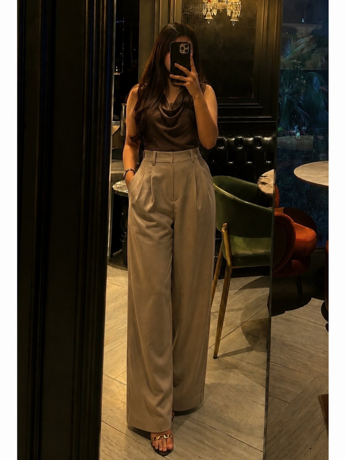 Woman in beige wide-leg trousers and brown top taking a mirror selfie indoors.
