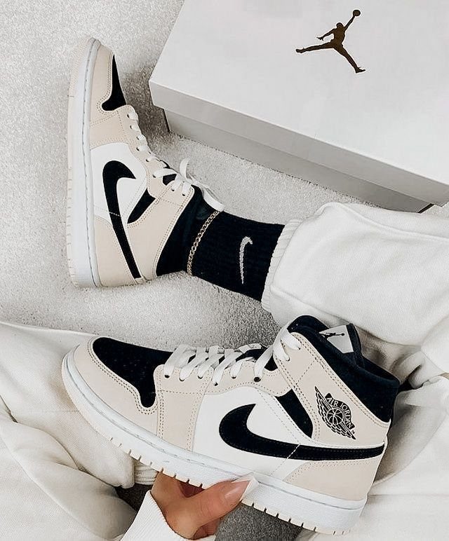 Beige and black leather high-top sneakers worn with white pants and black socks.