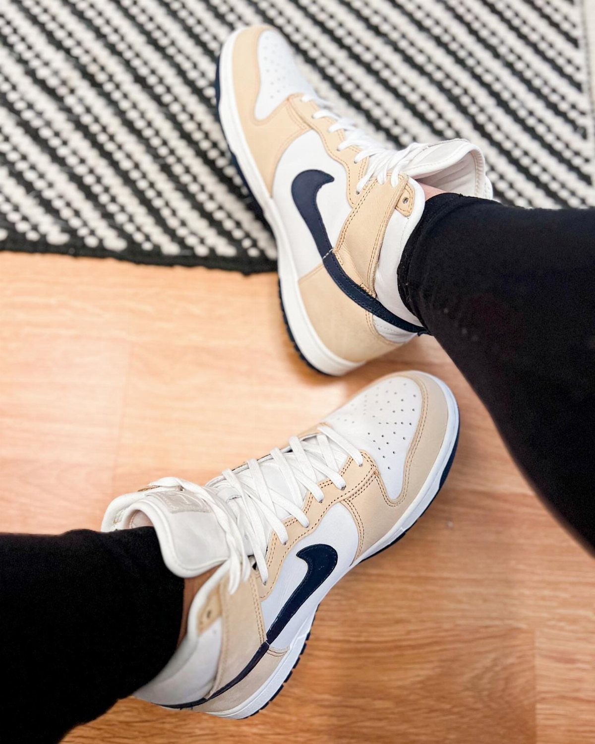 Beige and white leather high-top sneakers with dark blue swoosh on wooden floor