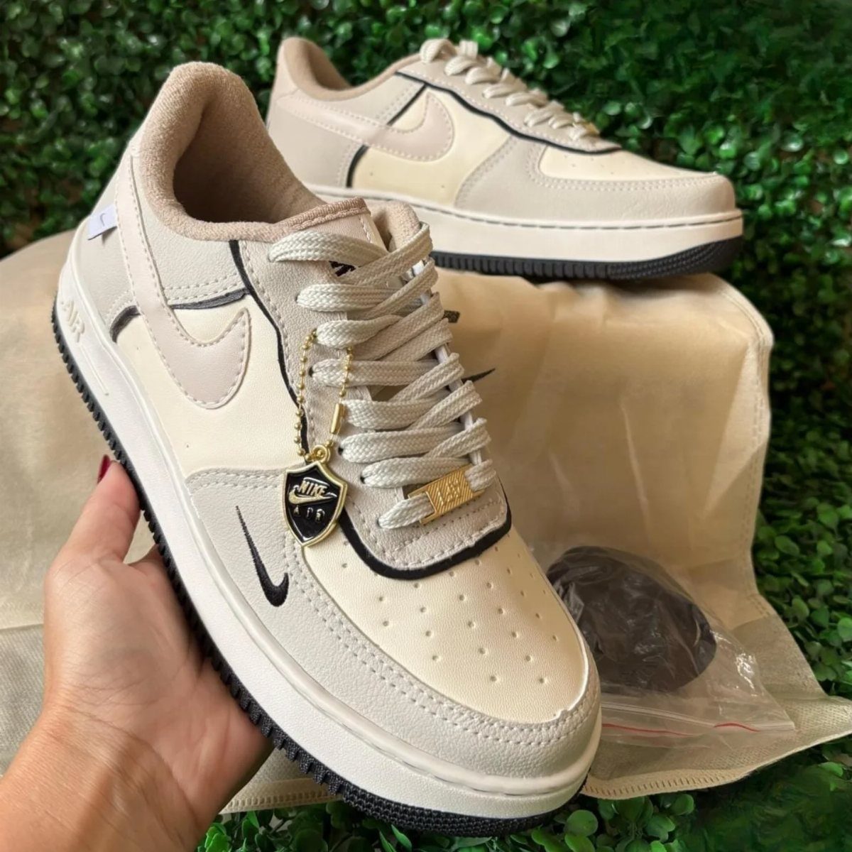 Beige leather sneakers with black accents and a gold Nike charm on greenery