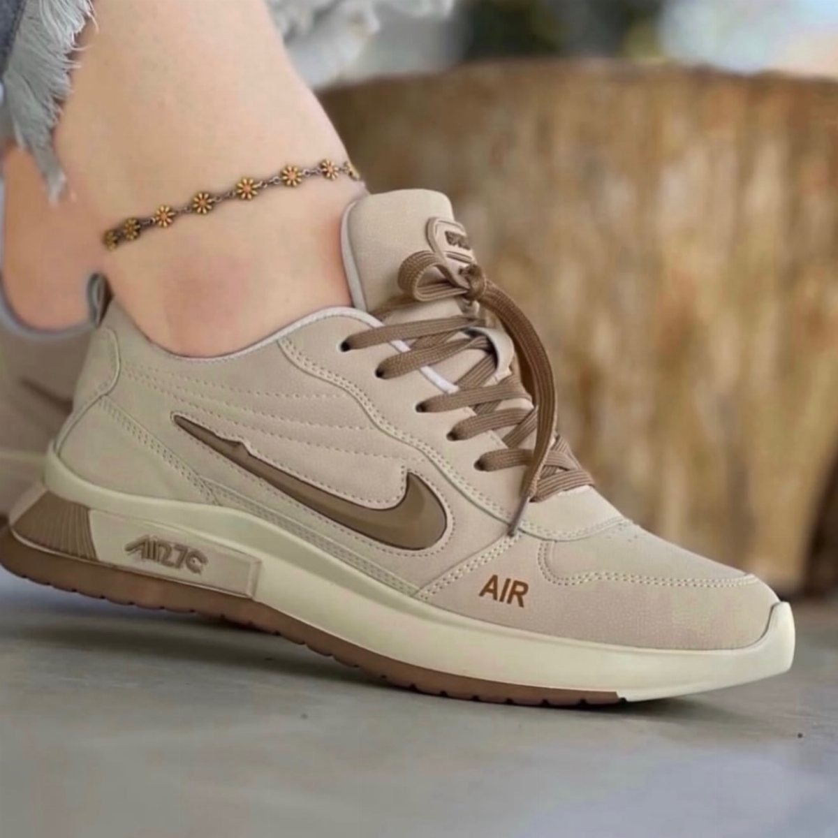 Beige Nike sneakers with brown swoosh and laces worn on a foot.