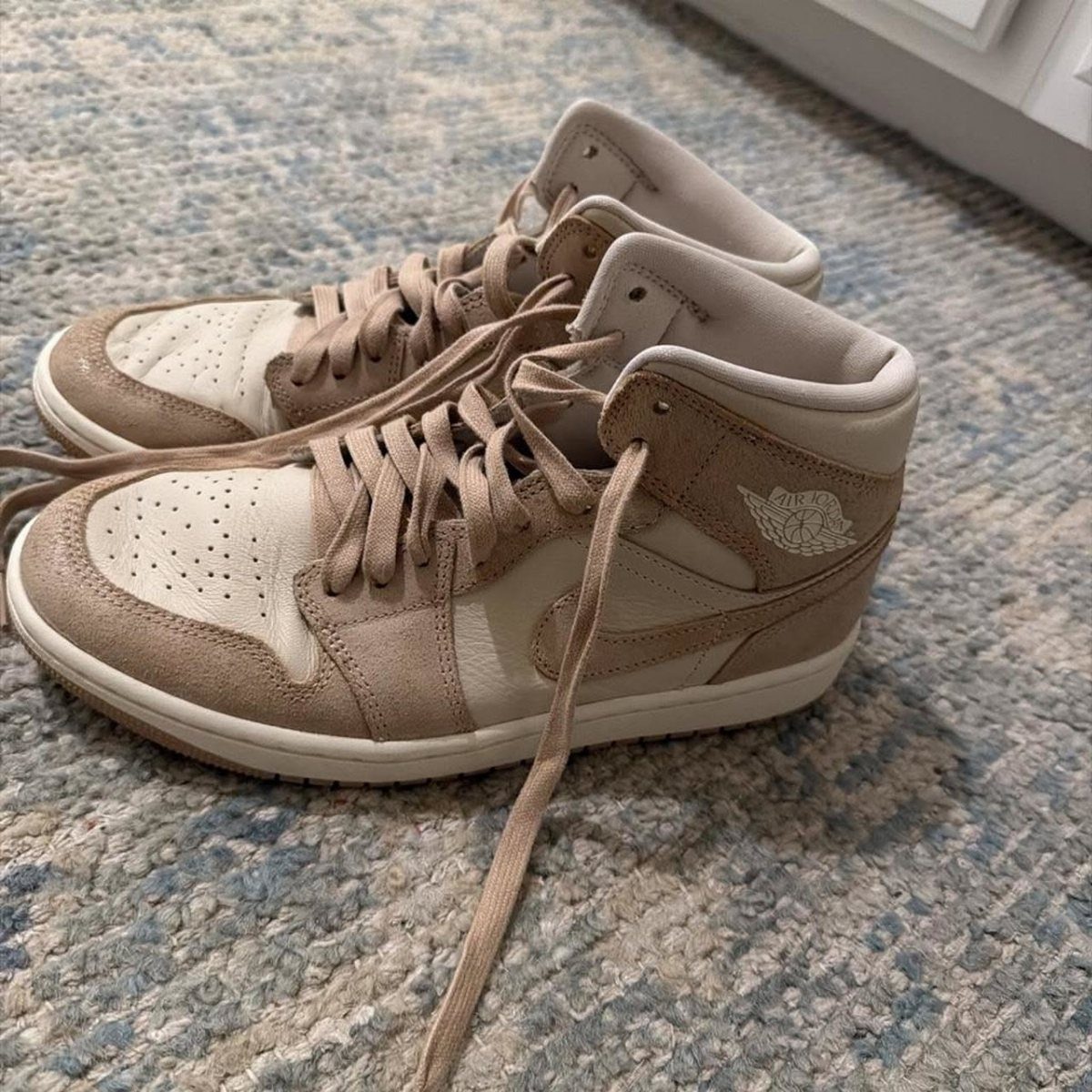 Beige suede and leather high-top sneakers resting on a textured blue carpet.