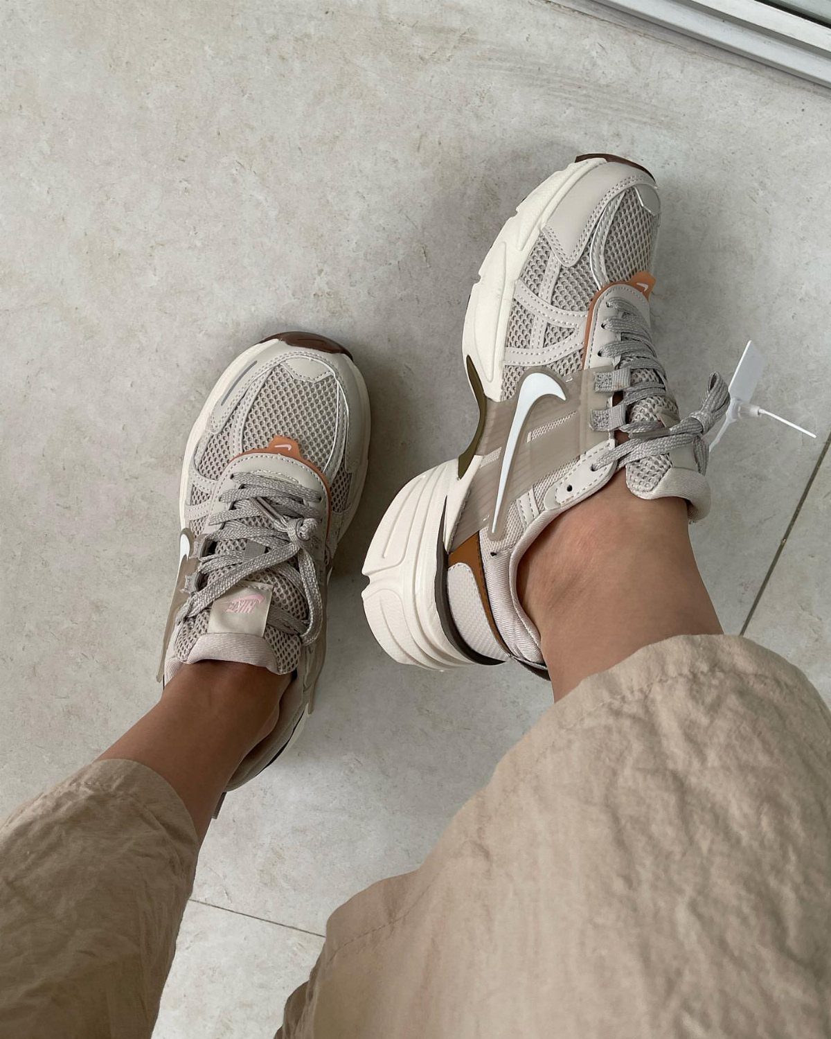 Nike Balance Shoes: 8 Sneaker Ideas for Women 5 Beige and white Nike sneakers worn with tan trousers on a stone floor