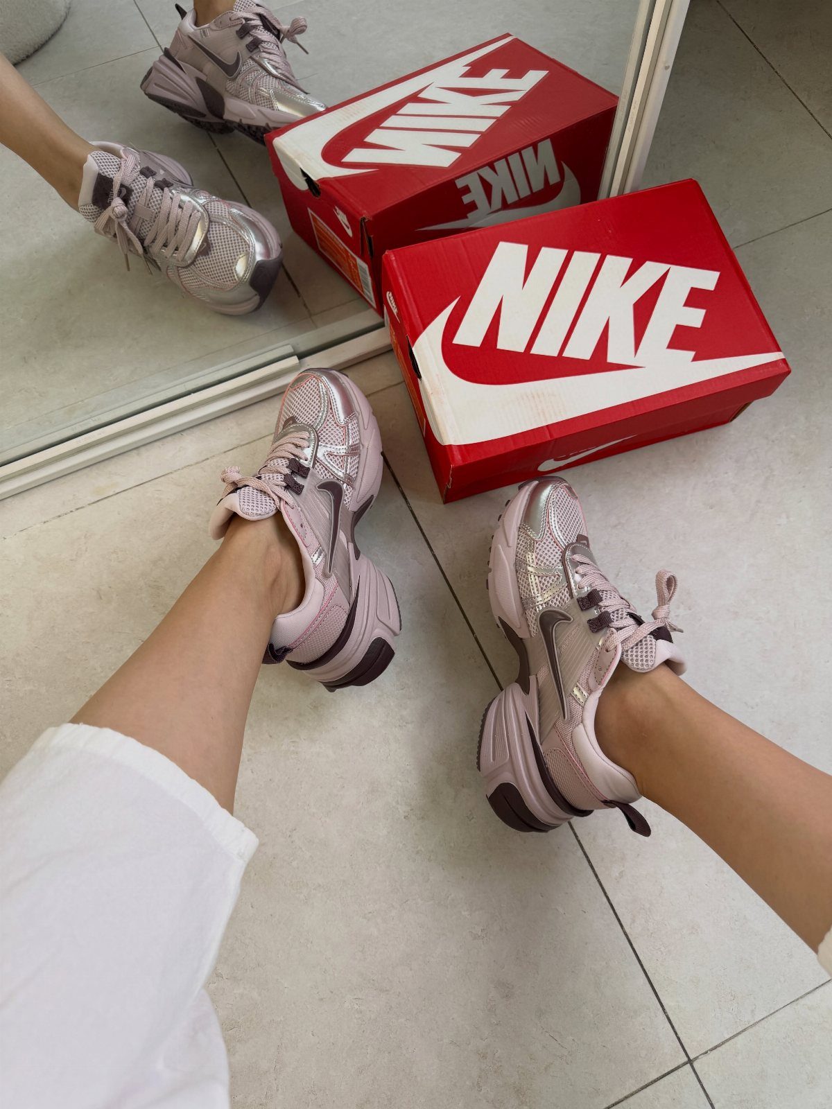 Nike Balance Shoes: 8 Sneaker Ideas for Women 8 Metallic pink Nike sneakers worn by a person next to red shoe boxes.