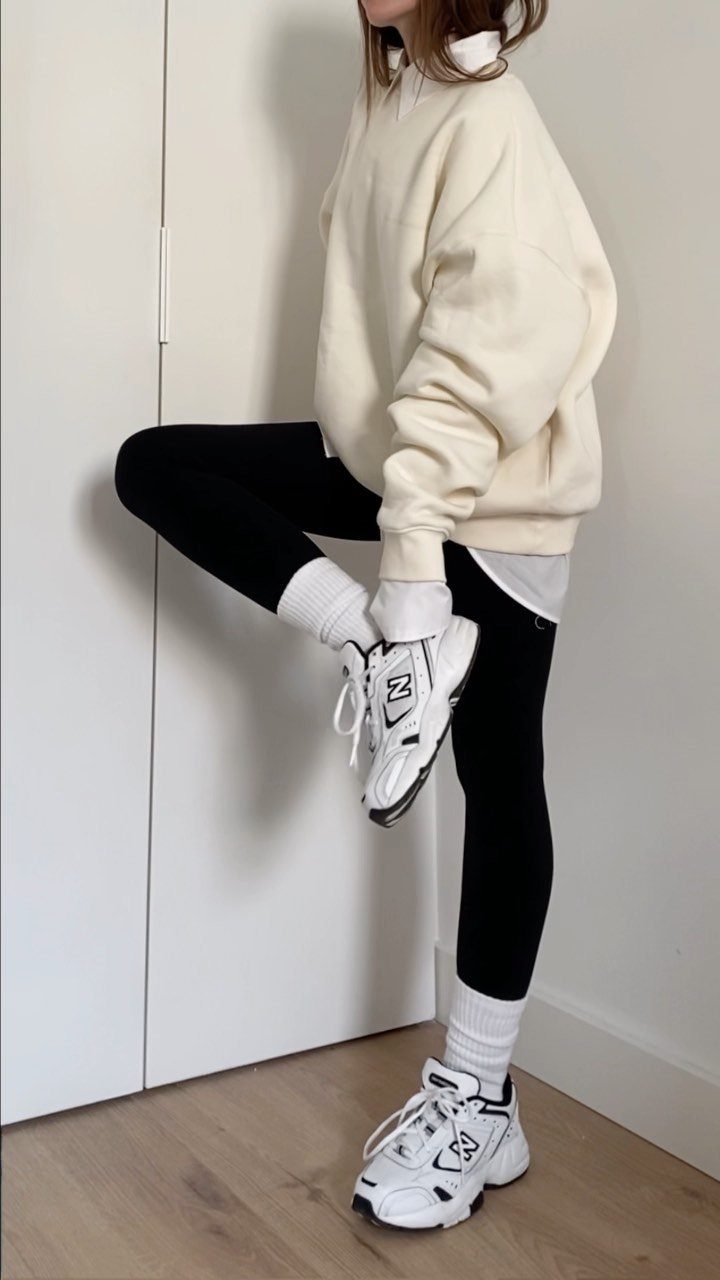 Nike Balance Shoes: 8 Sneaker Ideas for Women 2 Person wearing cream sweatshirt, black leggings, and white New Balance sneakers posing indoors.