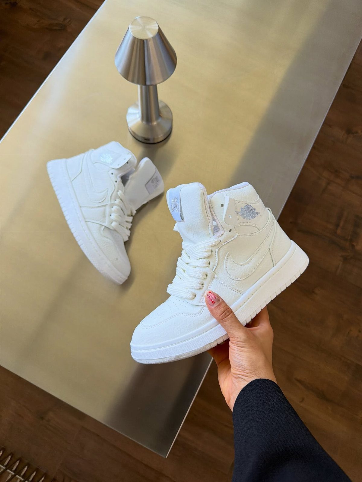 Nike Jordan Sneakers for Women: 12 Pairs to Know 10 White high-top Nike Jordan sneakers on a metallic table with a silver lamp.
