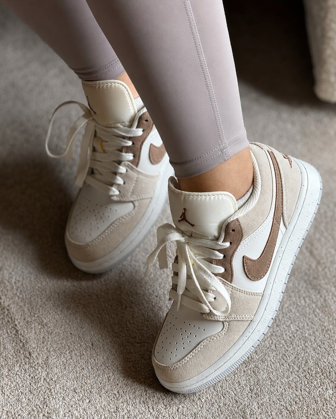 Nike Jordan Sneakers for Women: 12 Pairs to Know 11 Cream and tan Nike Air Jordan 1 sneakers worn with grey leggings on carpet.