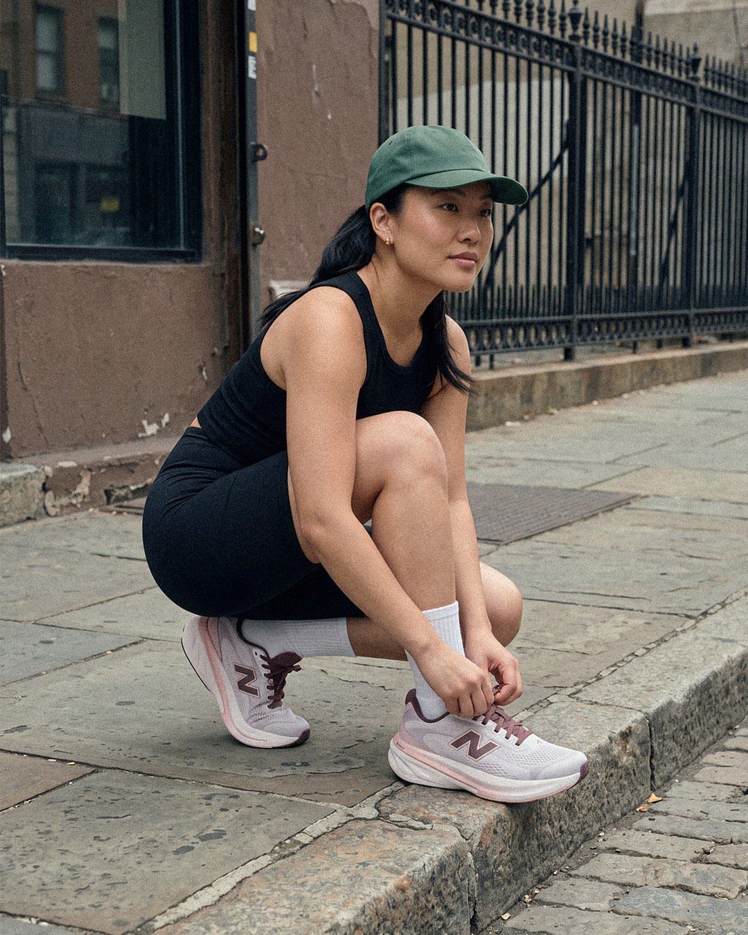 Woman in black athletic wear tying light purple New Balance sneakers on a sidewalk