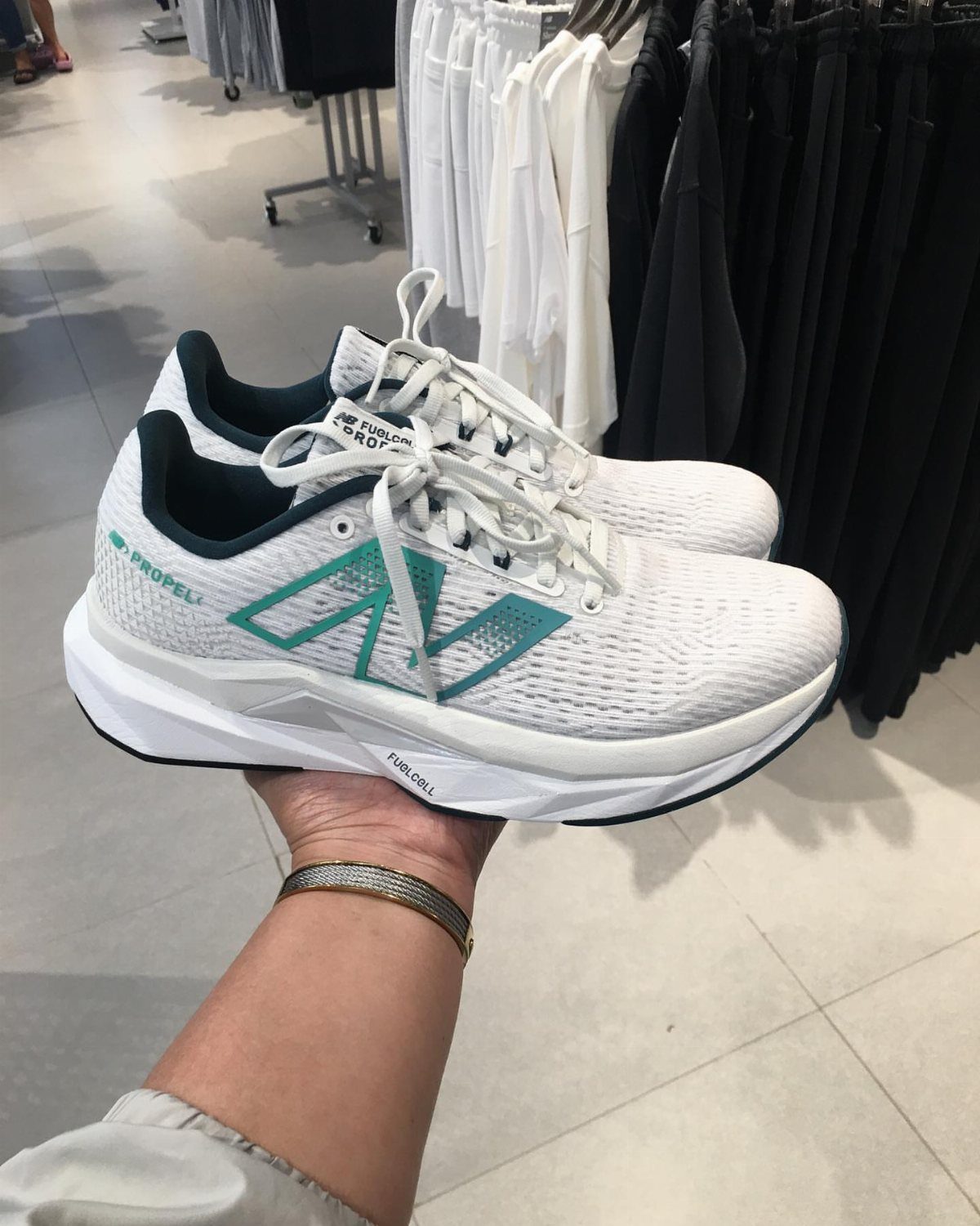 White New Balance FuelCell Propel sneakers with teal logos held in a hand.