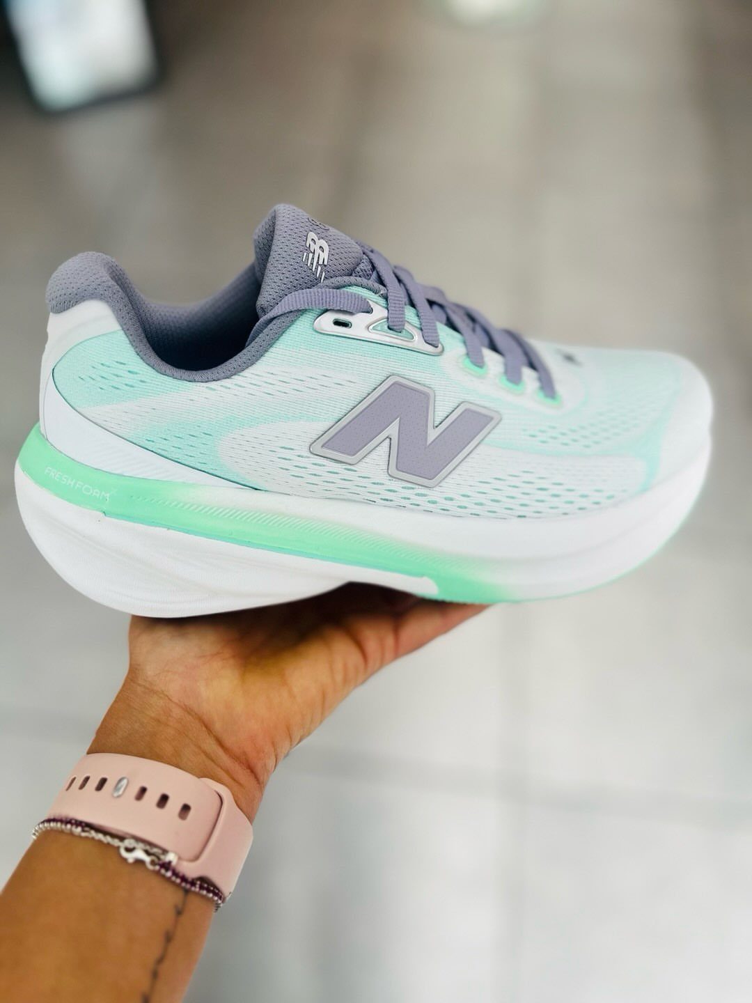 Mint green and white New Balance sneaker held by a hand against blurred background