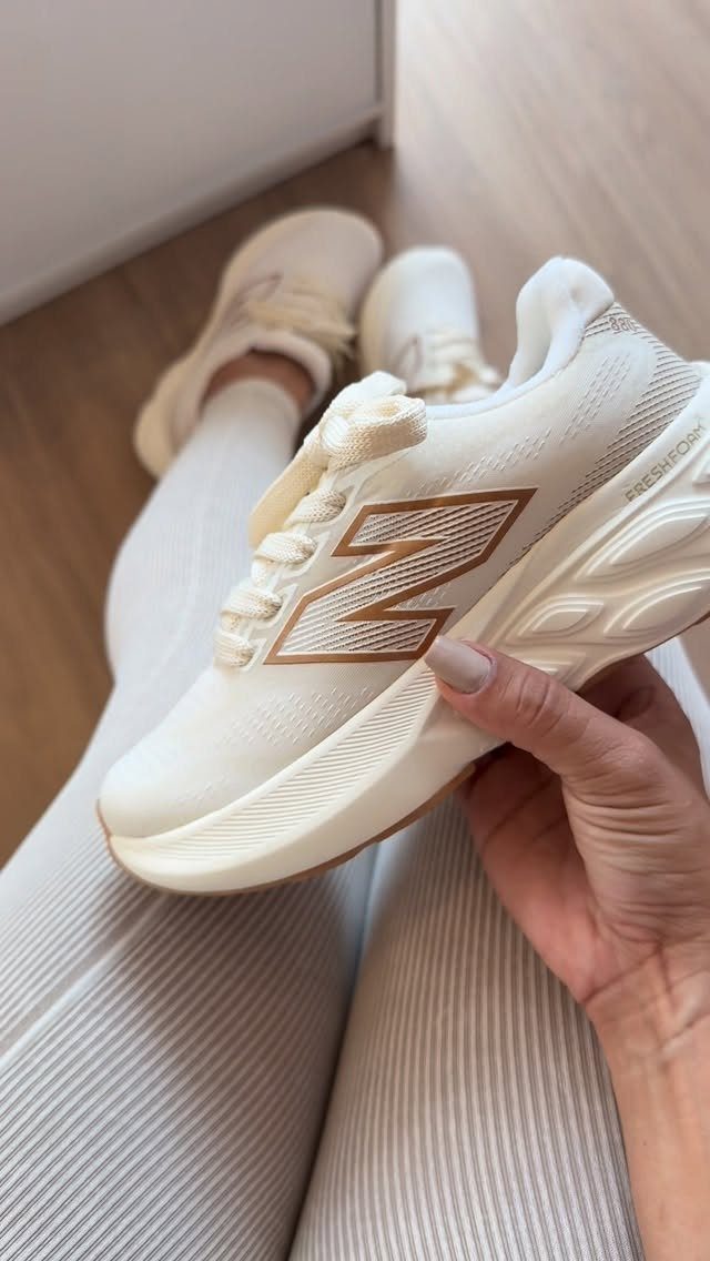 Cream New Balance sneakers with gold logos worn with white ribbed leggings.