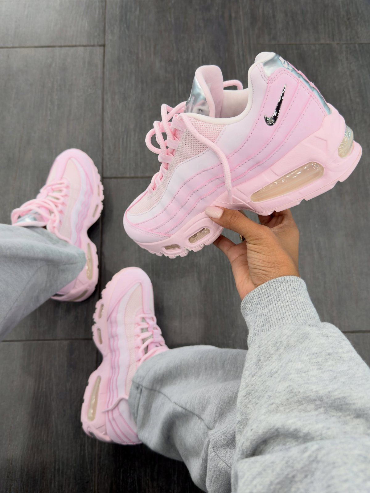 Pink Nike Air Max sneakers held by a person wearing grey sweatpants.