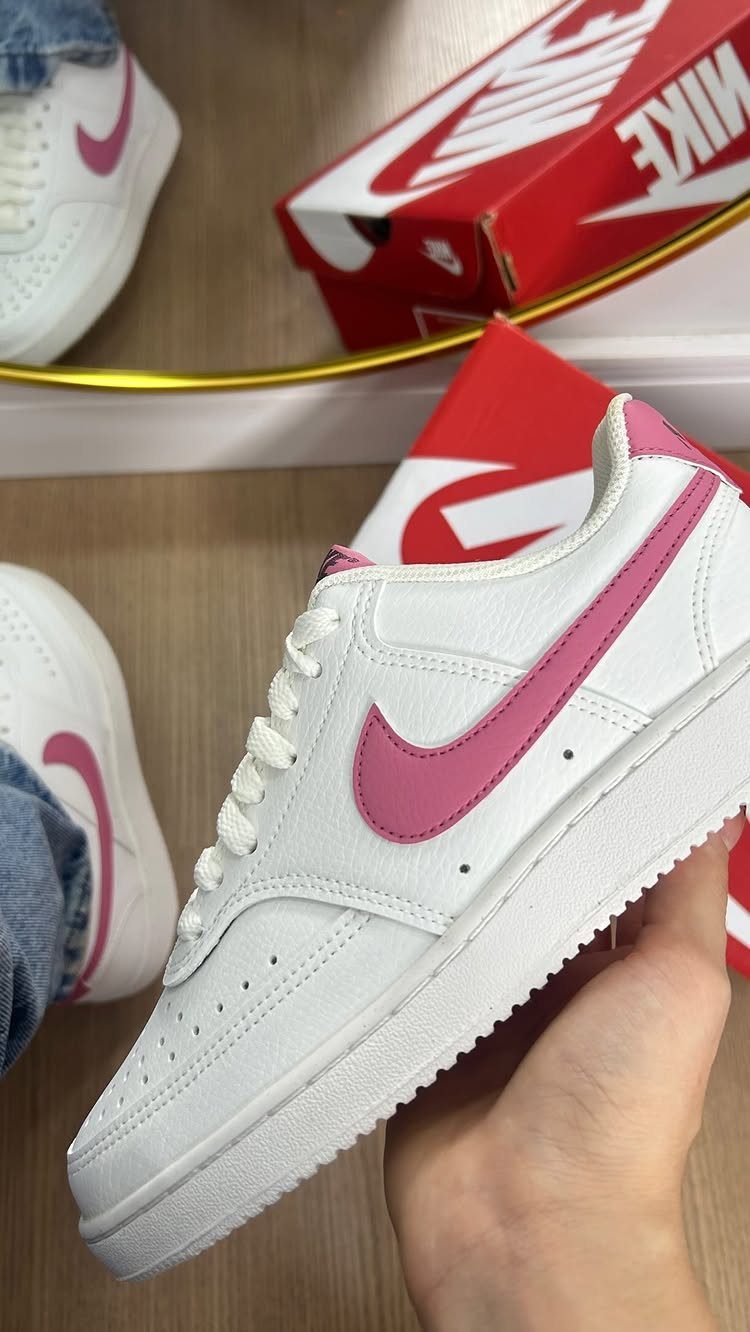 White Nike Court Vision sneakers with pink swoosh held against a red shoebox.