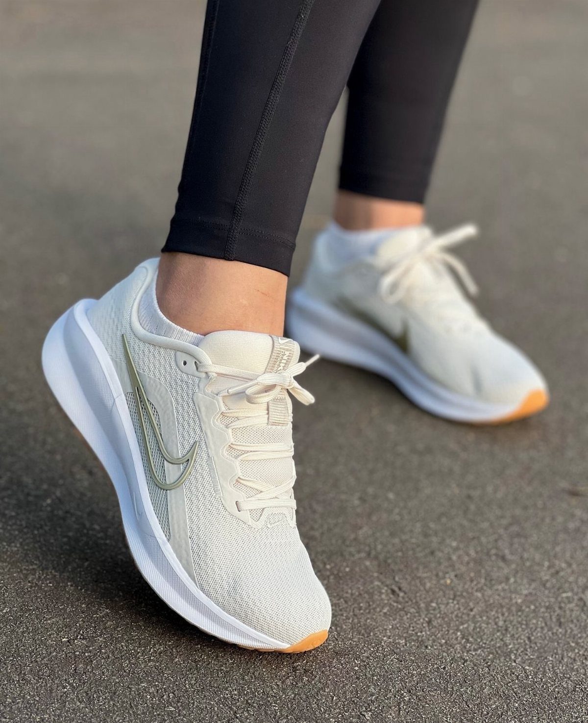 Off-white Nike running shoes with mesh uppers and black leggings on asphalt.