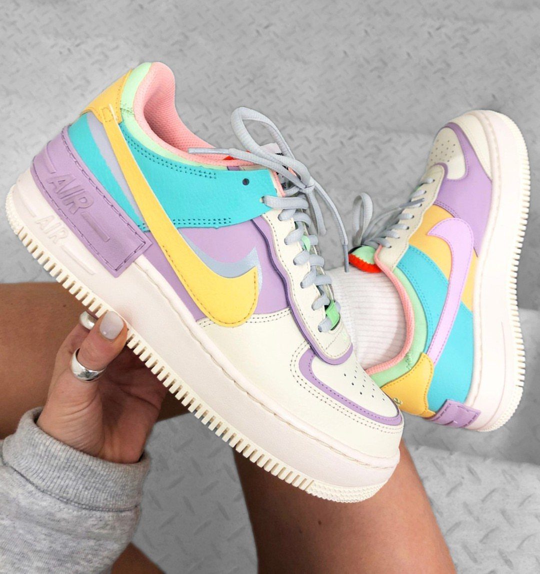 Nike sneakers with pastel yellow, purple, and blue accents held by a person.