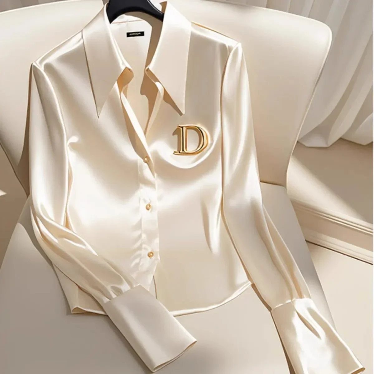 Champagne satin long-sleeve blouse with gold emblem draped over a white chair