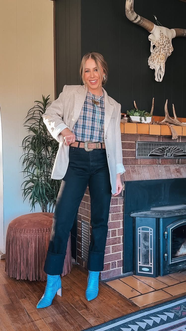 Woman in a beige blazer and light blue cowboy boots standing by a fireplace