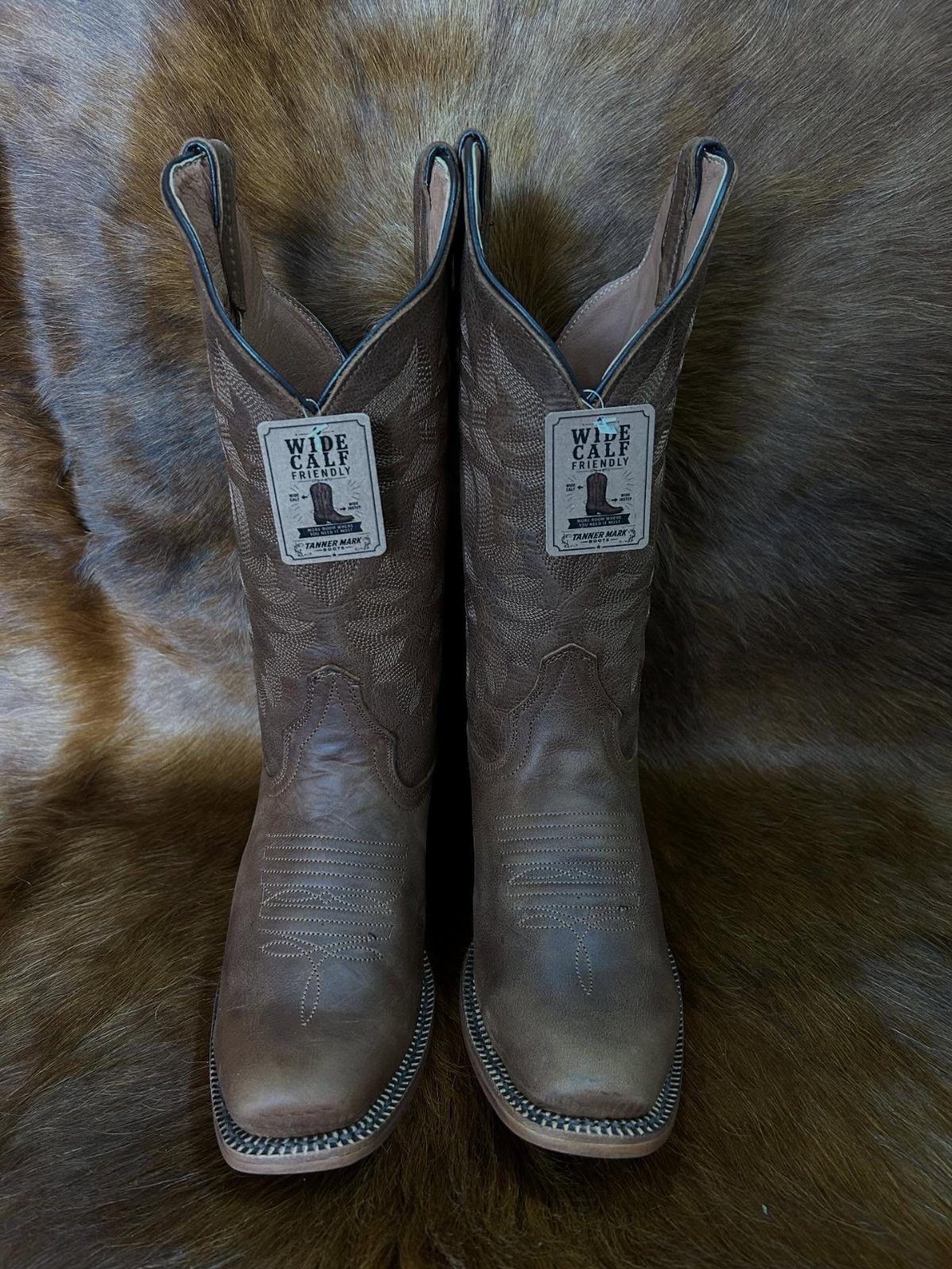 Brown leather cowboy boots with square toes resting on a brown fur rug.