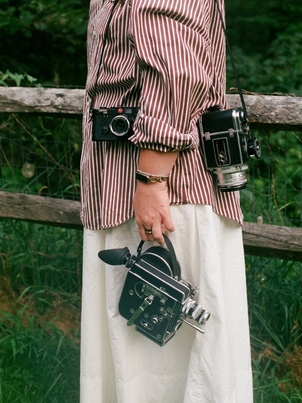 Three black vintage cameras carried by a person in a striped shirt.
